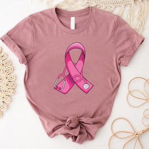 May include: A pink t-shirt with a pink ribbon and a stethoscope printed on the front. The ribbon is a symbol of breast cancer awareness.