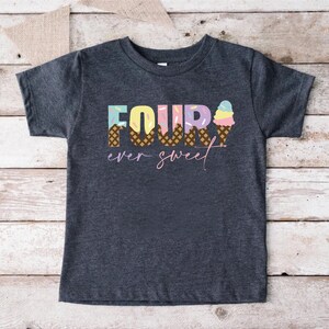 K&ouml;nnte beinhalten: Ein dunkelgraues T-Shirt mit dem Text "FOUR ever sweet" in bunten Buchstaben. Die Zahl vier besteht aus Eiswaffeln mit Streuseln.
