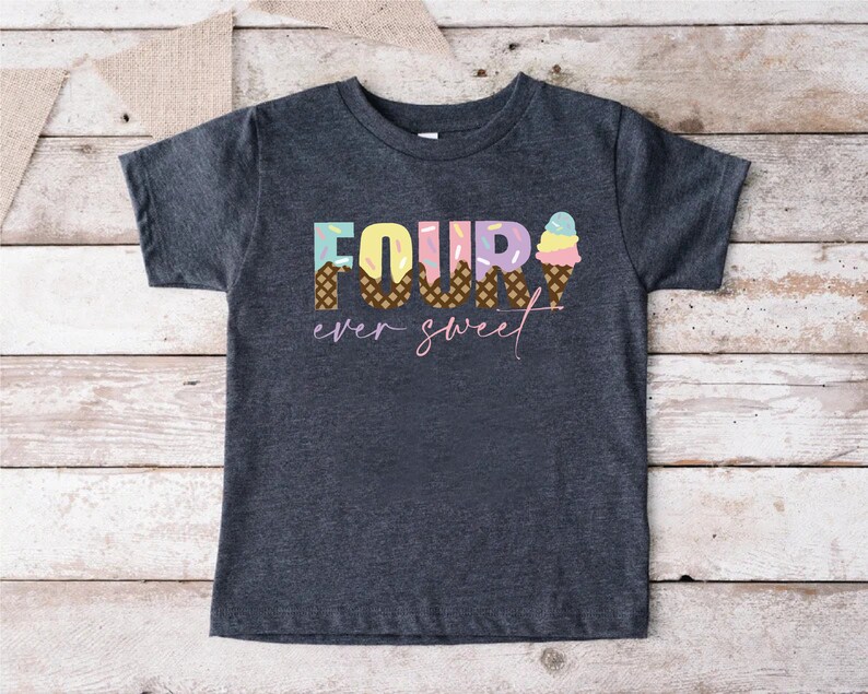 K&ouml;nnte beinhalten: Ein dunkelgraues T-Shirt mit dem Text "FOUR ever sweet" in bunten Buchstaben. Die Zahl vier besteht aus Eiswaffeln mit Streuseln.