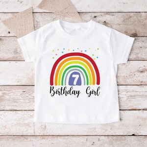 Peut inclure: T-shirt blanc avec un motif arc-en-ciel et le chiffre 7 dans un cercle bleu. Le texte "Birthday Girl" est &eacute;crit sous l'arc-en-ciel.