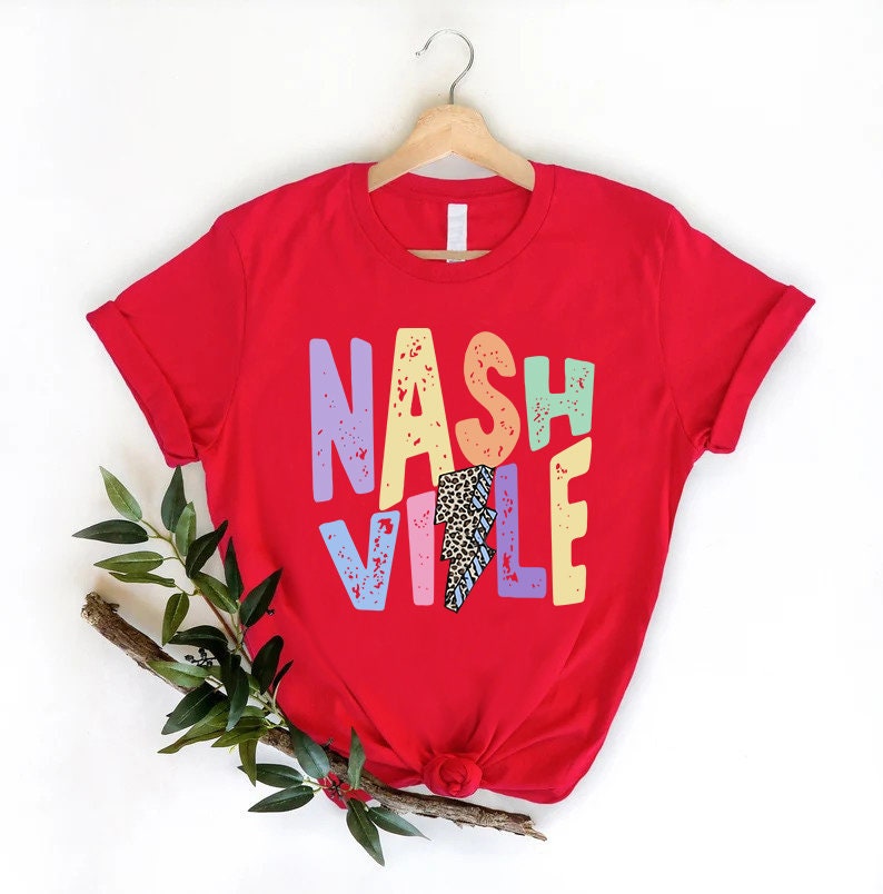 Puede incluir: Camiseta roja con un gr&aacute;fico colorido de "Nashville" que presenta un rayo con un dise&ntilde;o de estampado de leopardo.