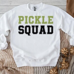 May include: White sweatshirt with the text "Pickle Squad" in black and green letters.