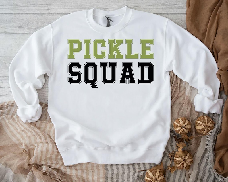 May include: White sweatshirt with the text "Pickle Squad" in black and green letters.