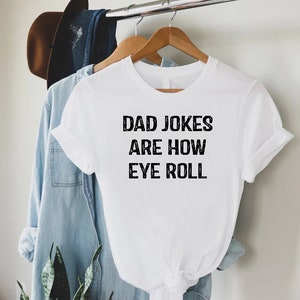May include: White t-shirt with black text that reads "Dad Jokes Are How Eye Roll".