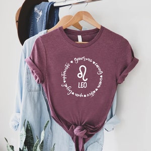 May include: A maroon t-shirt with a white circle design featuring the Leo zodiac symbol and the words "Leo", "generous", "caring", "active", "open", "loyal", and "optimistic".