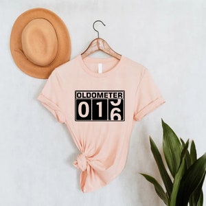 May include: A light pink t-shirt with a black graphic that says "Oldometer 016".