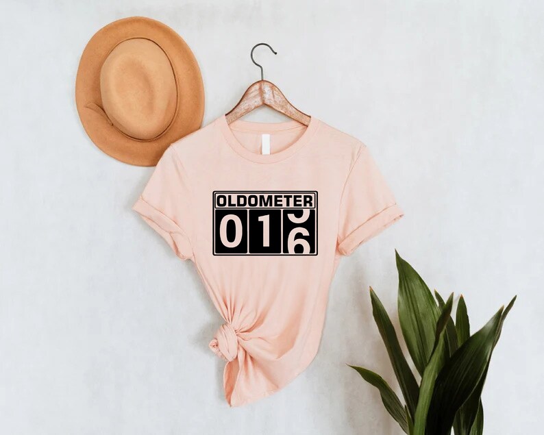 May include: A light pink t-shirt with a black graphic that says "Oldometer 016".
