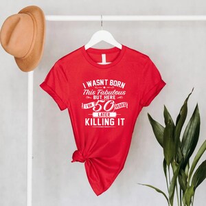 Pode incluir: Camiseta vermelha com texto branco que diz "Eu n&atilde;o nasci assim, mas aqui estou, 50 anos depois e estou arrasando".