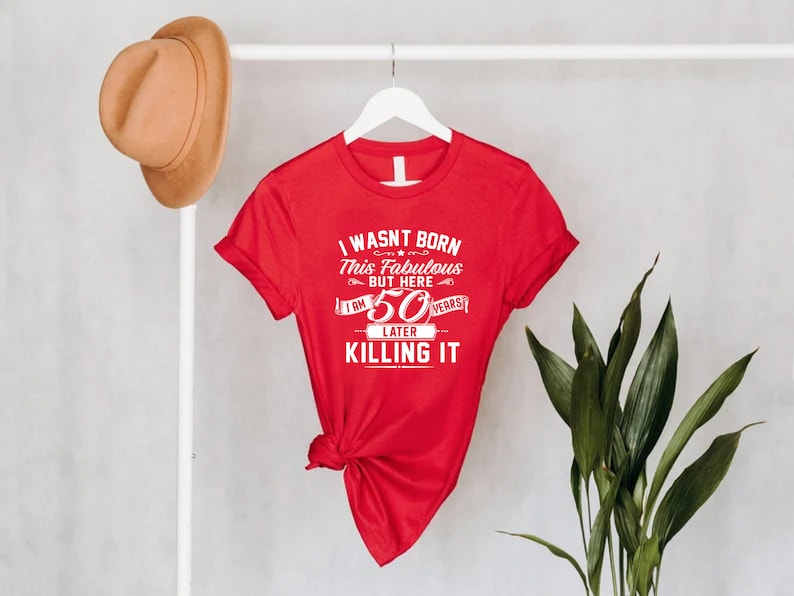Pode incluir: Camiseta vermelha com texto branco que diz "Eu n&atilde;o nasci assim, mas aqui estou, 50 anos depois e estou arrasando".