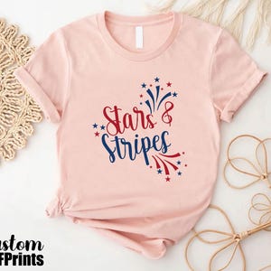 May include: A pink t-shirt with a red, white, and blue graphic that says "Stars & Stripes" with a firework design.