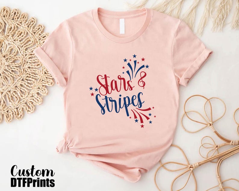 May include: A pink t-shirt with a red, white, and blue graphic that says "Stars & Stripes" with a firework design.