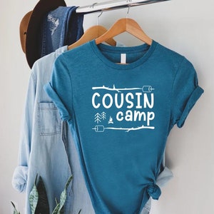 May include: A teal blue t-shirt with white text that reads "COUSIN camp" with a campfire, trees, and marshmallows graphic.