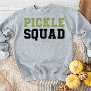 May include: A gray sweatshirt with the text "PICKLE SQUAD" in black and green letters.