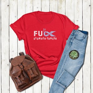 May include: Red t-shirt with a white graphic that says "F**k Stomach Cancer" with a purple ribbon.