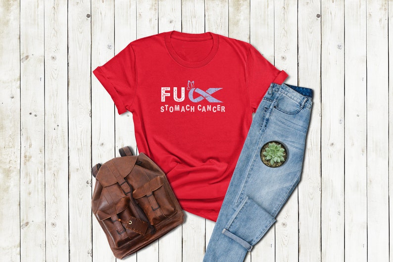 May include: Red t-shirt with a white graphic that says "F**k Stomach Cancer" with a purple ribbon.