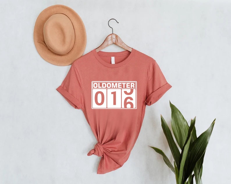 May include: A coral coloured t-shirt with a white graphic that says "Oldometer 016".