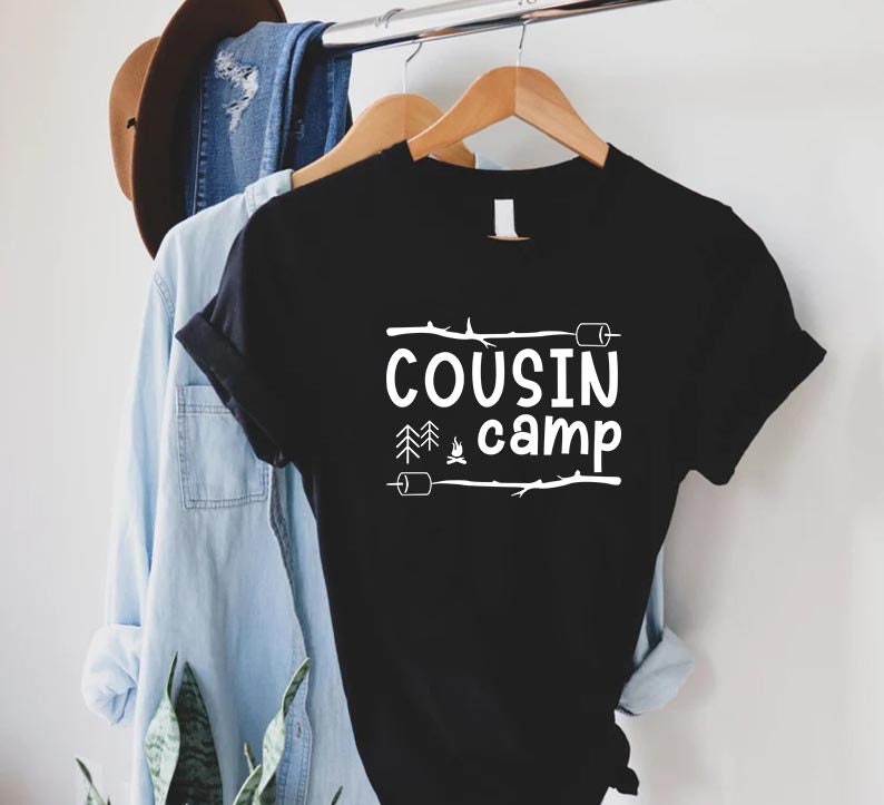 May include: Black t-shirt with white text that reads "COUSIN camp" with a campfire, trees, and marshmallows graphic.