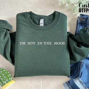Puede incluir: Una sudadera verde oscuro con el texto "I'M NOT IN THE MOOD" impreso en blanco en la parte delantera.