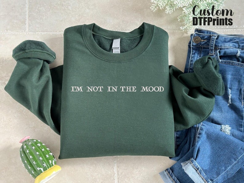 Puede incluir: Una sudadera verde oscuro con el texto "I'M NOT IN THE MOOD" impreso en blanco en la parte delantera.