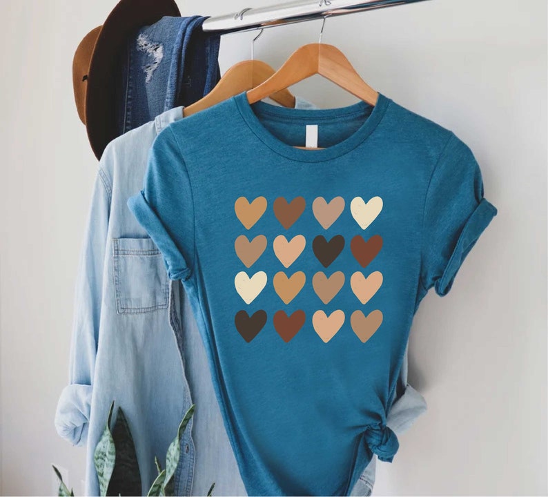 May include: A teal blue t-shirt with a graphic of a grid of 16 hearts in various shades of brown, beige, and cream.
