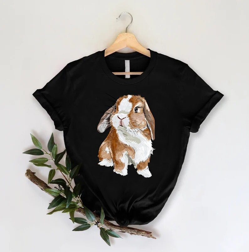 K&ouml;nnte beinhalten: Schwarzes T-Shirt mit einer Illustration eines braunen und wei&szlig;en Kaninchens.