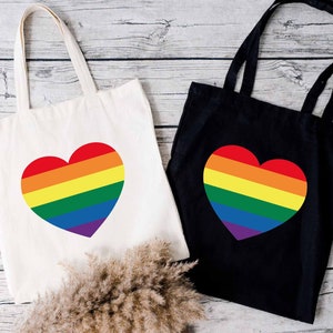 May include: Two tote bags with rainbow heart designs. One bag is white and the other is black.