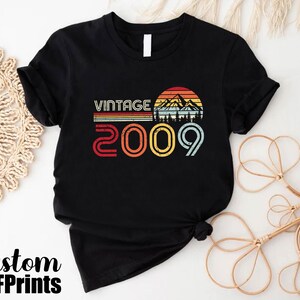 May include: Black t-shirt with a vintage design featuring a mountain range and the text "Vintage 2009".
