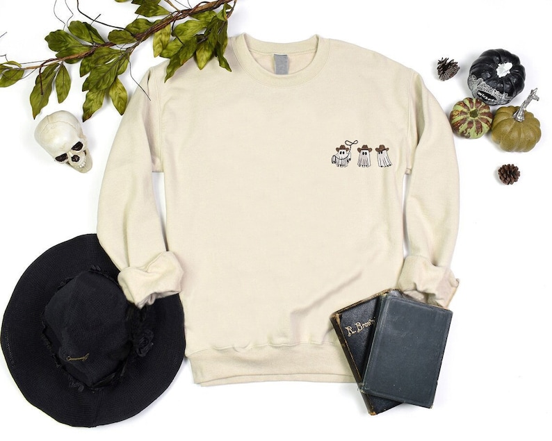 a white sweater with embroidered three cowboy boo ghosts on it