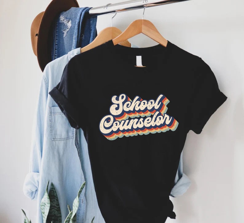 May include: A black t-shirt with the words 'School Counselor' in a retro rainbow font.