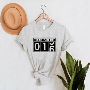 May include: Grey t-shirt with a black and white graphic that says "Oldometer 016".