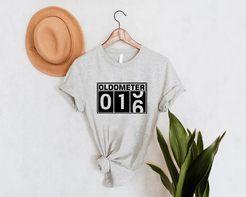May include: Grey t-shirt with a black and white graphic that says "Oldometer 016".