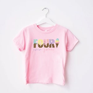 K&ouml;nnte beinhalten: Rosa T-Shirt mit kurzen &Auml;rmeln und dem Text "FOUR" in bunten Buchstaben, die mit Eiswaffeln und Streuseln verziert sind. Der Text "ever sweet" steht unter dem Wort "FOUR".