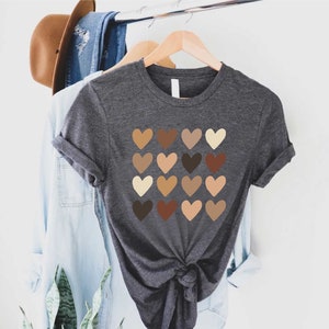 May include: A dark gray t-shirt with a design of 16 different colored hearts. The hearts are arranged in a grid pattern and represent different skin tones.