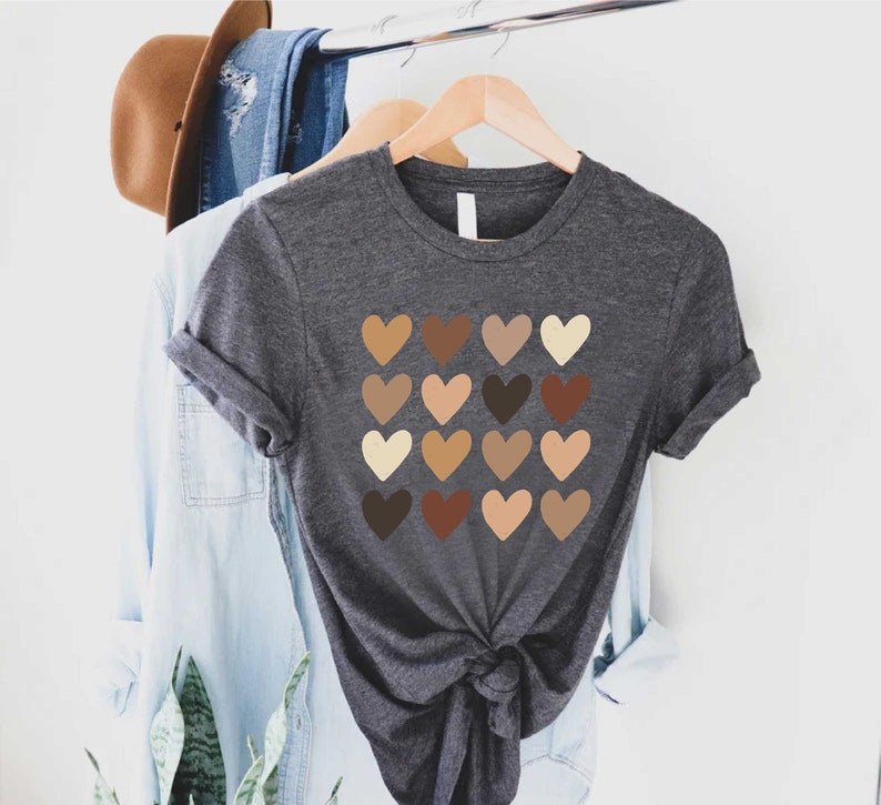 May include: A dark gray t-shirt with a design of 16 different colored hearts. The hearts are arranged in a grid pattern and represent different skin tones.