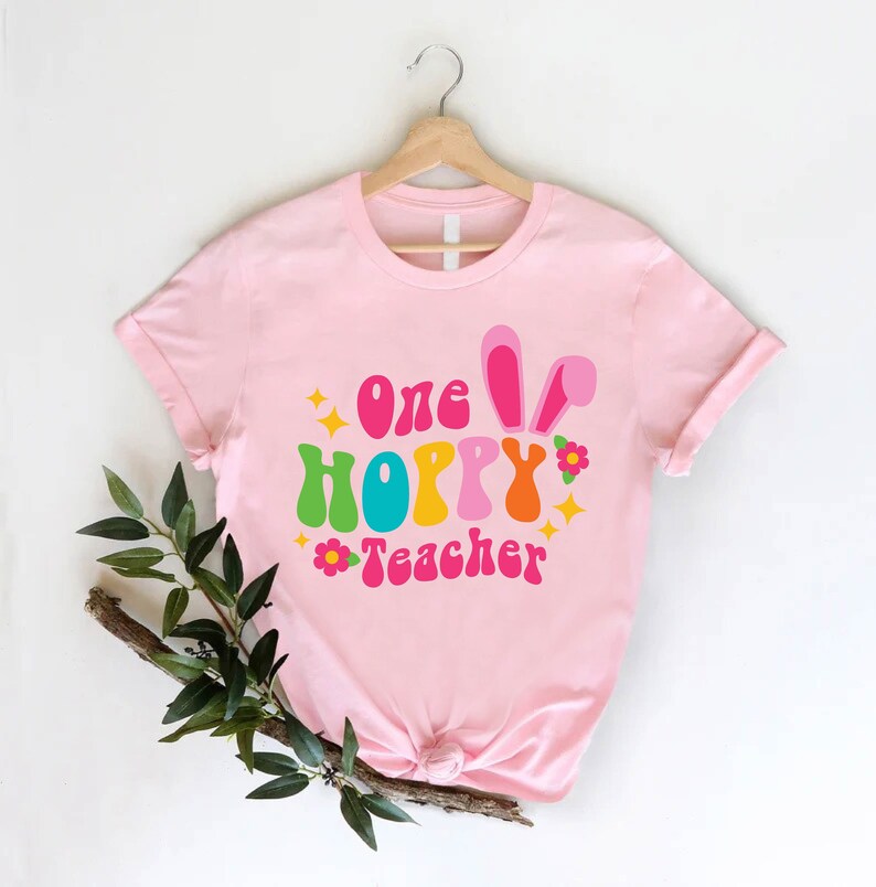 May include: Pink t-shirt with the text "one hoppy teacher" in colourful retro font with bunny ears and flowers.