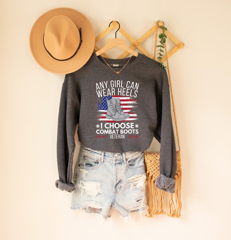 May include: Gray sweatshirt with a white graphic that says "Any girl can wear heels * I choose combat boots * Veteran" with an American flag and a pair of combat boots.