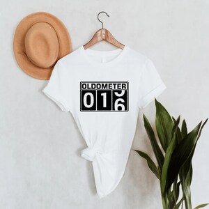 May include: White t-shirt with black text that reads "Oldometer 016".