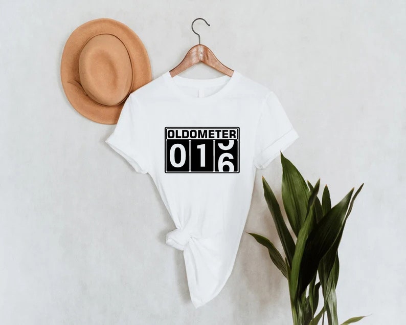 May include: White t-shirt with black text that reads "Oldometer 016".