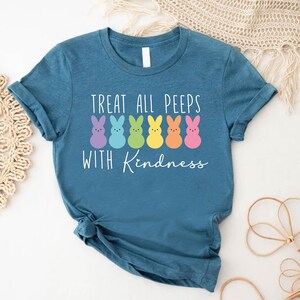 May include: Teal blue t-shirt with a white graphic of a line of colourful marshmallow Peeps with the text "Treat all peeps with kindness".