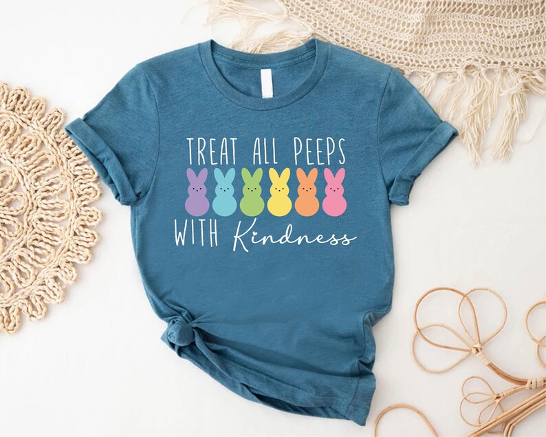 May include: Teal blue t-shirt with a white graphic of a line of colourful marshmallow Peeps with the text "Treat all peeps with kindness".