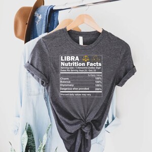 May include: Gray t-shirt with a white graphic that says "LIBRA Nutrition Facts" and lists the zodiac sign's traits, including charm, balance, diplomacy, and dangerous when provoked.