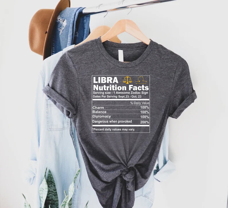 May include: Gray t-shirt with a white graphic that says "LIBRA Nutrition Facts" and lists the zodiac sign's traits, including charm, balance, diplomacy, and dangerous when provoked.