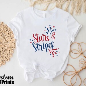 May include: White t-shirt with a red, white, and blue graphic that says "Stars & Stripes".