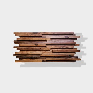 May include: A wall decor made of reclaimed wood planks arranged in a staggered pattern. The planks are various shades of brown and have a rustic, weathered look.