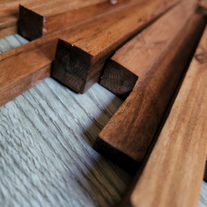 May include: Close-up of a wooden wall art piece made of multiple thin strips of wood arranged in a geometric pattern. The wood has a rich brown color and a natural grain.