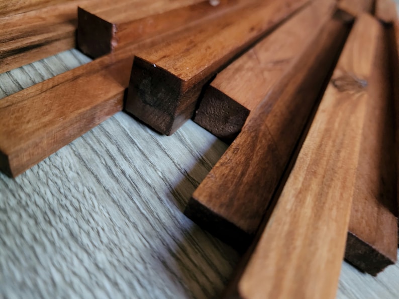 May include: Close-up of a wooden wall art piece made of multiple thin strips of wood arranged in a geometric pattern. The wood has a rich brown color and a natural grain.