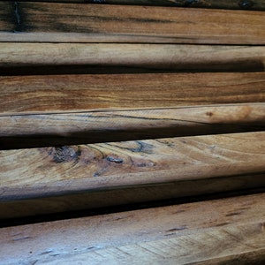 May include: Close-up of a wall made of stacked wooden planks. The planks are arranged in a staggered pattern, creating a textured surface. The wood is a rich brown color with darker streaks and knots.