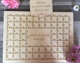 May include: A wooden heart-shaped puzzle guest book with the text "Without you our puzzle isn't complete. Please sign a piece." and "Nicole & David 14.02.2022".