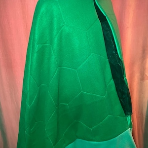May include: Green fleece cape with a quilted turtle shell design. The cape has a teal collar and trim.