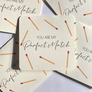 May include: A card with the text "You are my Perfect Match" in black script font. The background is cream colored with a pattern of red-tipped matchsticks.